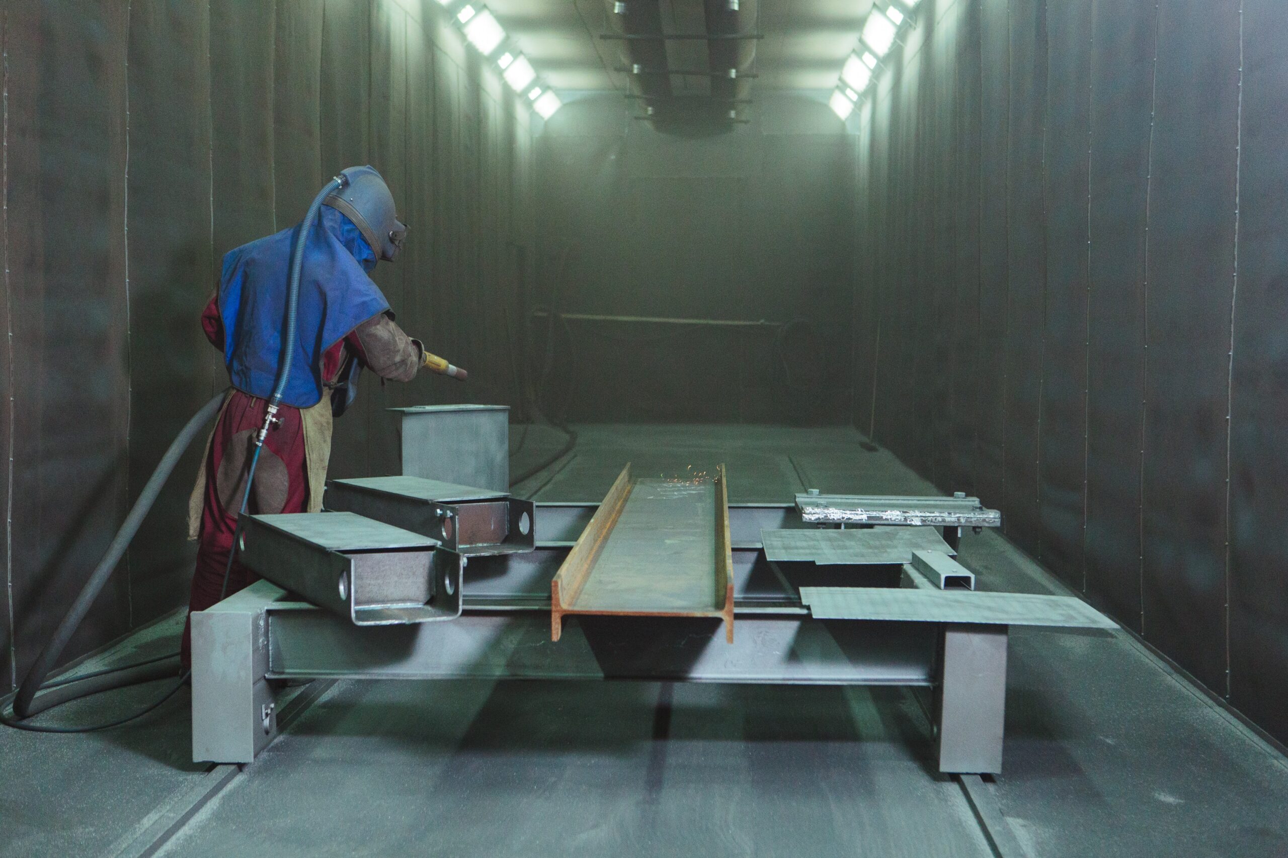 A worker in full protective gear engaging in abrasive blasting, emphasizing the need for a dust collector and fume extractor.