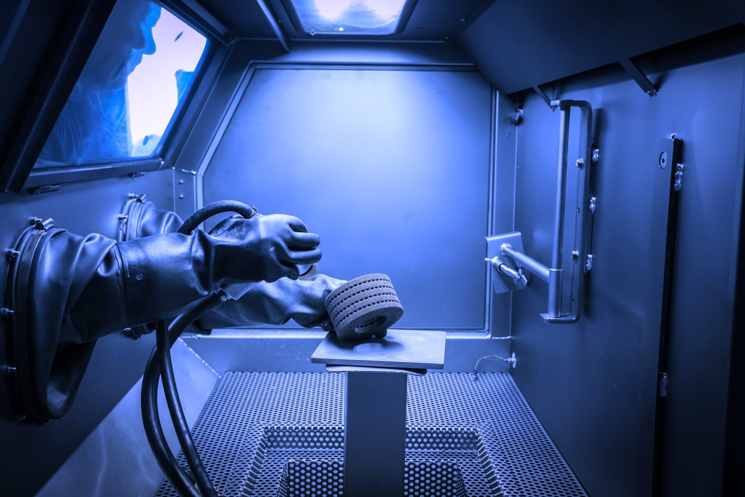 A worker in gloves performing detailed abrasive work, emphasizing the importance of a dust collector and fume extractor.